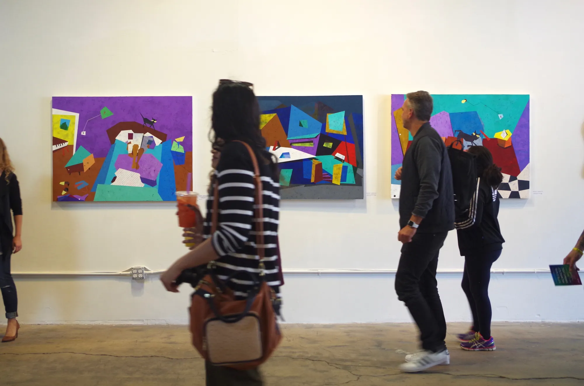 Visitors at an exhibition, walking past three of the paintings