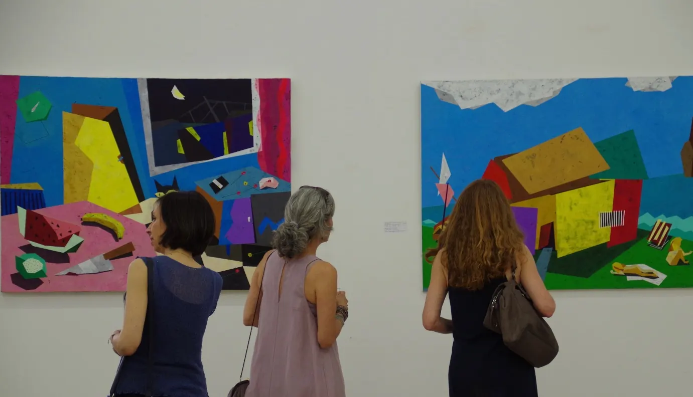 Three visitors looking at two of the paintings at an exhibition